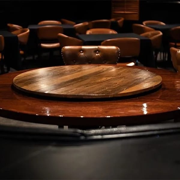 Dark restaurant interior with a large round wooden table and brown leather chairs.