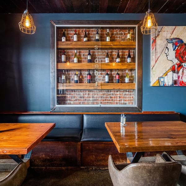 Cozy restaurant interior with wooden tables, black booths, brick walls, and a wine display.