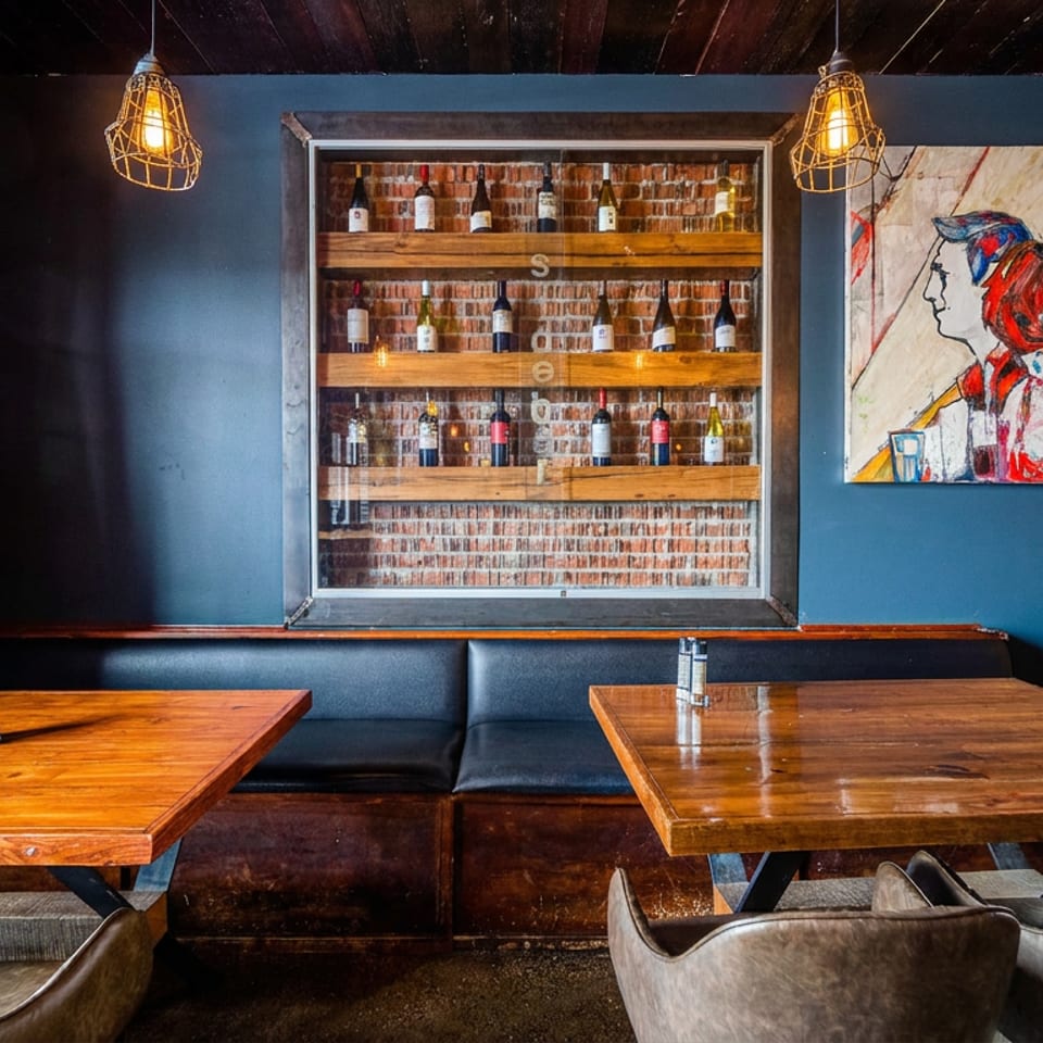 Cozy restaurant interior with wooden tables, black booths, brick walls, and a wine display.