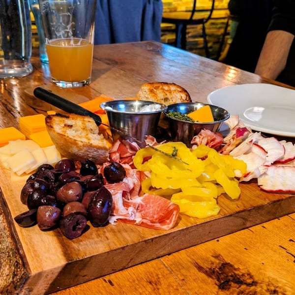 A charcuterie board with cheeses, meats, olives, peppers, and bread on a rustic wooden table.