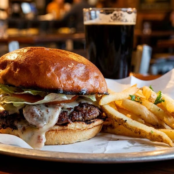 Cheeseburger with fries and a dark beer on a metal plate in a restaurant setting.