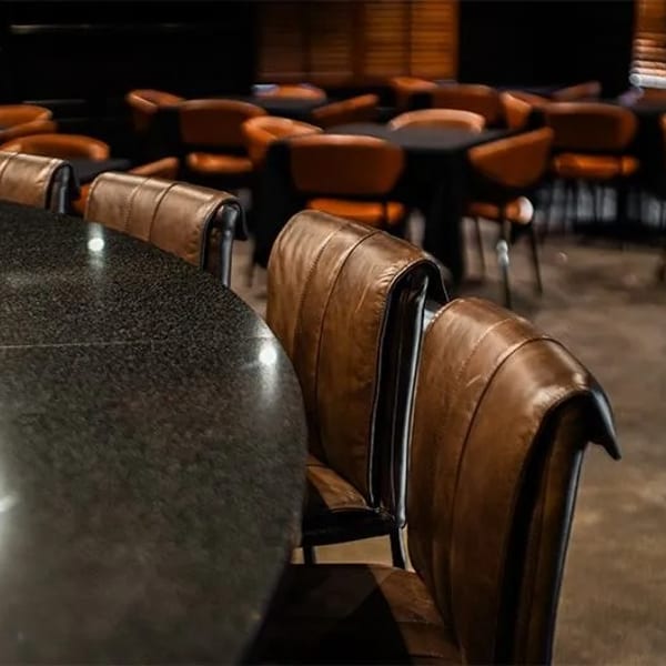 Dark restaurant interior with a black granite table and brown leather chairs in the foreground.