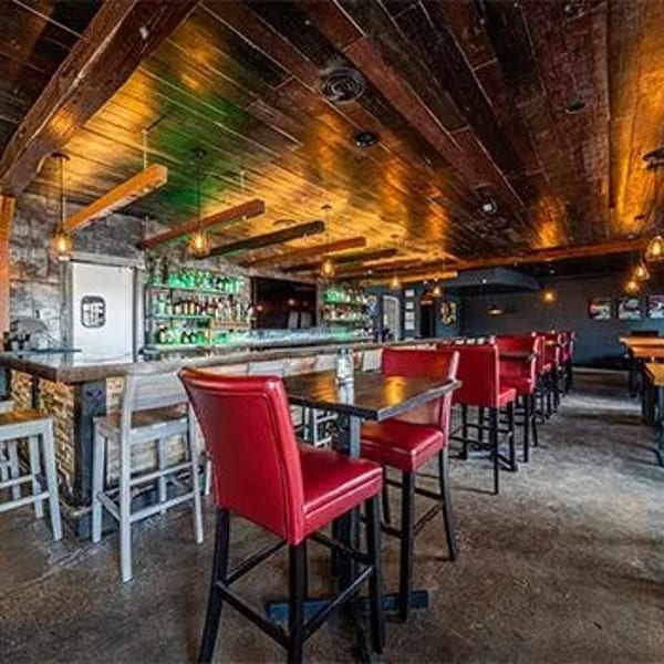 A rustic bar interior with a long wooden bar, red bar stools, and exposed wooden beams.