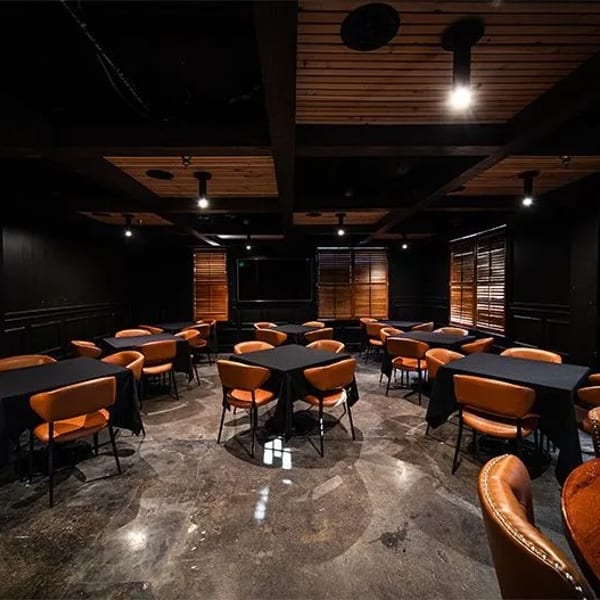 Dark dining room with black tables, orange chairs, wooden blinds, and a concrete floor.