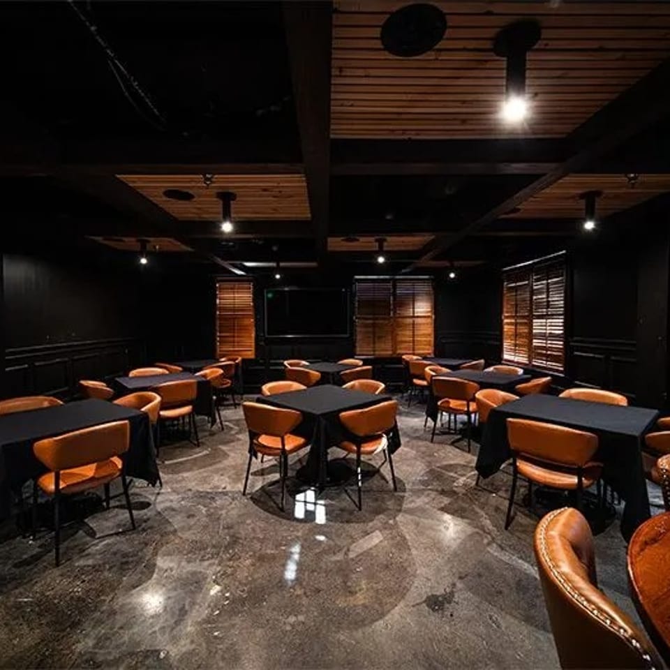 Dark dining room with black tables, orange chairs, wooden blinds, and a concrete floor.