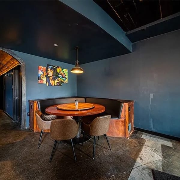 A dark, moody restaurant interior with a corner booth, round table, and pop art on the wall.